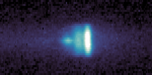 A wide, rectangular, pixelated image with a dark purple background. Near the right side, there is a bright, elongated cluster of pixels that transition from white at the center to light blue and then darker blue as they extend leftward. Fainter blue and purple pixels form a tapered shape stretching further to the left. The rest of the image is filled with dark purple and black pixels.